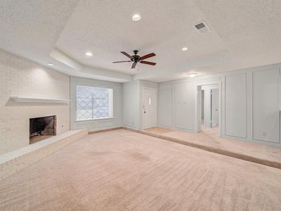 Unfurnished living room featuring a textured ceiling, a brick fireplace, ceiling fan, a tray ceiling, and light colored carpet | Image 3