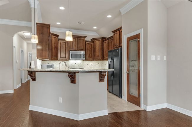 Kitchen with stainless steel microwave, black fridge, a breakfast bar, a peninsula, and light stone counters | Image 17