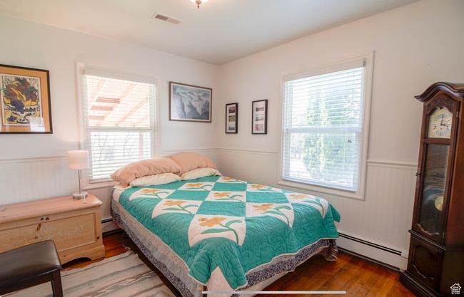 Bedroom with a baseboard heating unit, multiple windows, wainscoting, and wood finished floors | Image 21