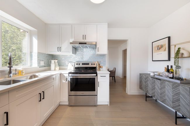Kitchen with light countertops, under cabinet range hood, electric stove, backsplash, and a sink | Image 16