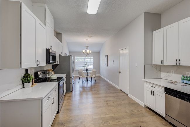 Kitchen featuring stainless steel appliances, a chandelier, a textured ceiling, white cabinets, and light wood finished floors | Image 8