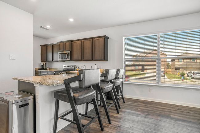 Kitchen with baseboards, stainless steel appliances, dark brown cabinets, luxury vinyl plank floors, and a breakfast bar area | Image 7