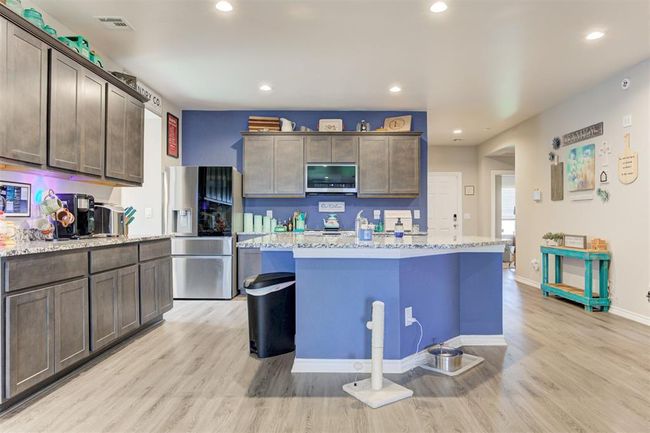 Kitchen featuring appliances with stainless steel finishes, light wood-style flooring, light stone counters, a center island, and dark brown cabinets | Image 12