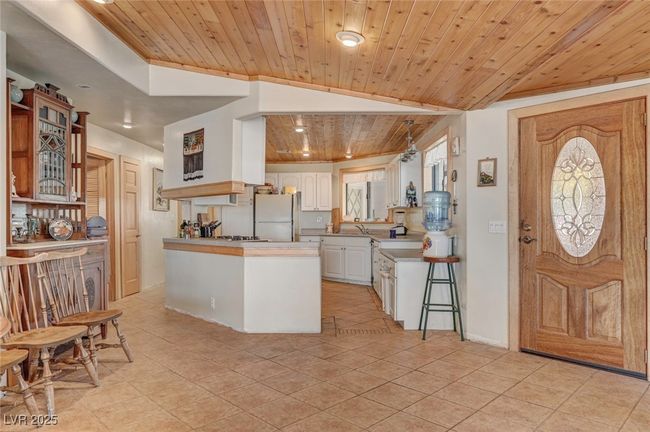 Kitchen with freestanding refrigerator, wooden ceiling, glass insert cabinets, a peninsula, and white cabinetry | Image 28