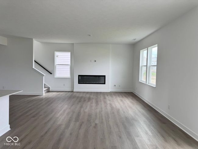 unfurnished living room with wood finished floors, stairway, and a glass covered fireplace | Image 6