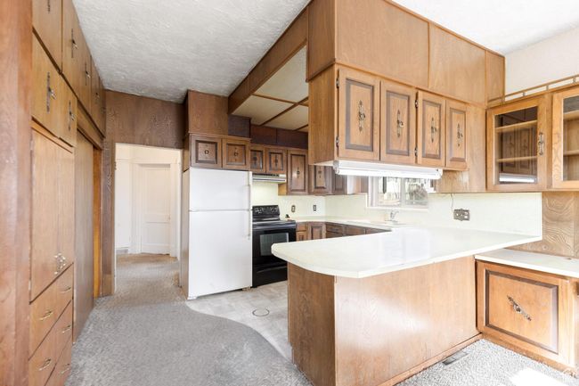 Kitchen featuring light countertops, freestanding refrigerator, a peninsula, under cabinet range hood, and electric range | Image 23