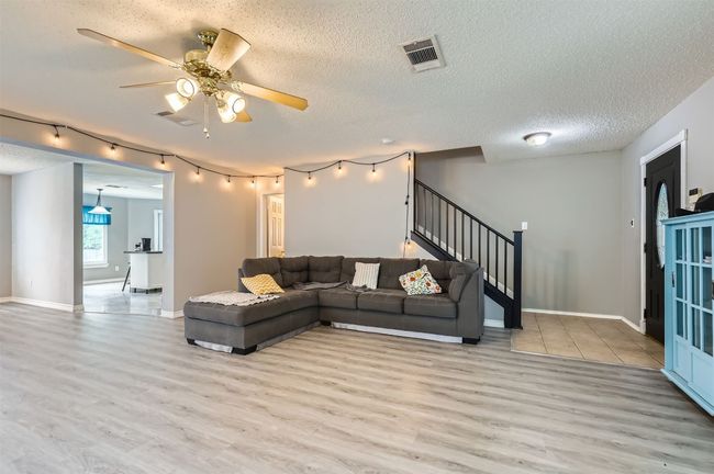 Living area with light wood finished floors, stairs, ceiling fan, baseboards, and a textured ceiling | Image 7
