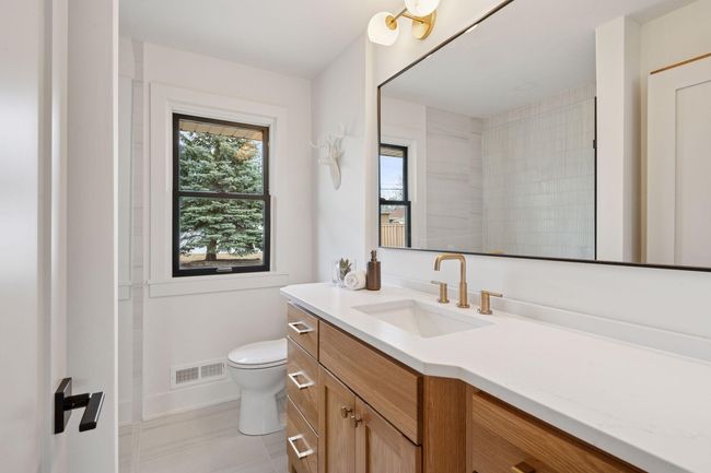 Main level bathroom offers white oak cabinetry, upgraded faucets & counters along with a zero edge shower. | Image 16