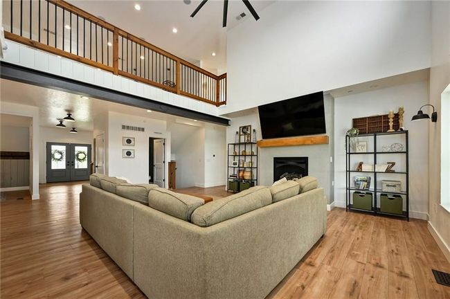 Living room featuring ceiling fan, a fireplace, baseboards, light lip flooring, and a high ceiling | Image 17