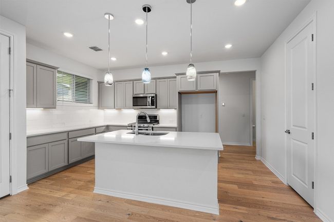 Kitchen featuring 42" cabinets, under-cabinet task lighting, painted cabinets in a light gray/sage green, crisp white subway tile and a large breakfast bar with pendant lights. Quartz countertops and stainless appliances | Image 6