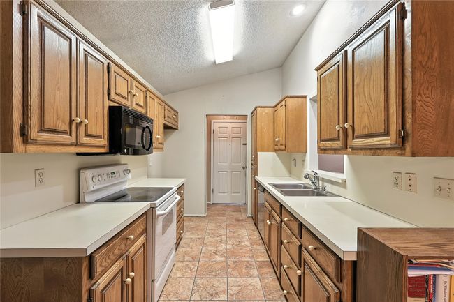 Kitchen with white electric range oven, vaulted ceiling, light countertops, a textured ceiling, and brown cabinets | Image 17