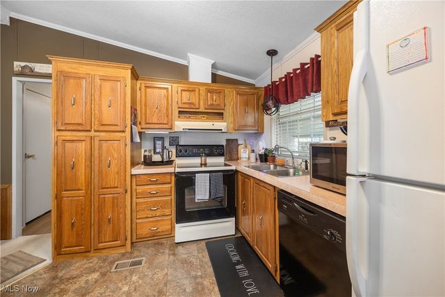 Kitchen with white appliances, ornamental molding, vaulted ceiling, ventilation hood, and light countertops | Image 24
