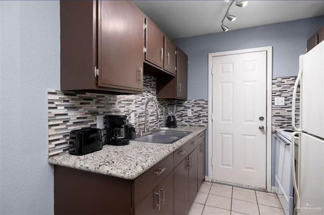 Kitchen with light countertops, freestanding refrigerator, light tile patterned floors, backsplash, and dark brown cabinets | Image 6