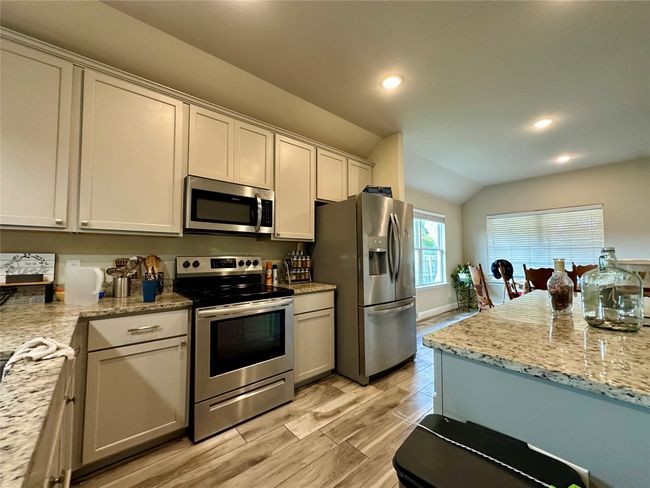 Kitchen with appliances with stainless steel finishes, recessed lighting, lofted ceiling, light stone counters, and light wood finished floors | Image 16