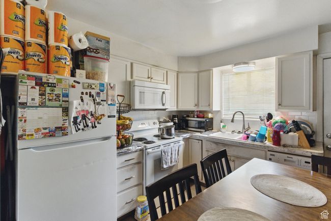 Kitchen featuring white cabinets, backsplash, light countertops, a sink, and white appliances | Image 24