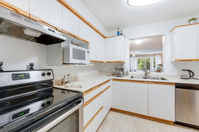 Kitchen featuring stainless steel appliances, a sink, under cabinet range hood, white cabinets, and light countertops | Image 15