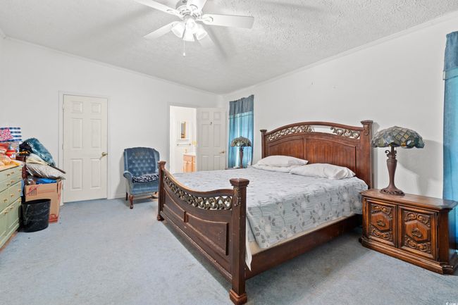 Carpeted bedroom featuring a textured ceiling, ceiling fan, ensuite bathroom, lofted ceiling, and crown molding | Image 12