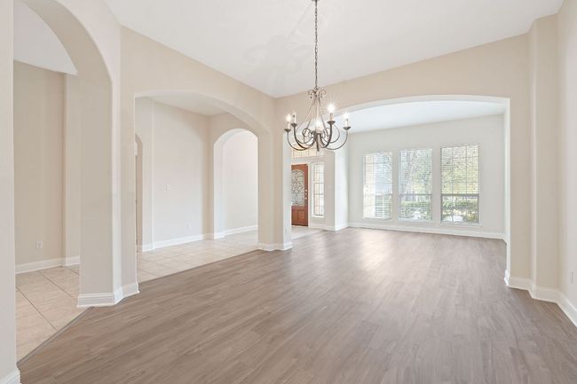 Empty room featuring light wood-style flooring, baseboards, a notable chandelier, and arched walkways | Image 7