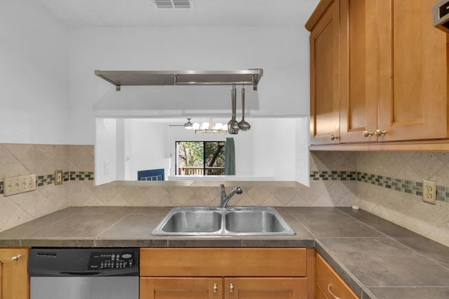 Kitchen featuring decorative backsplash, dishwasher, dark countertops, a sink, and brown cabinetry | Image 4