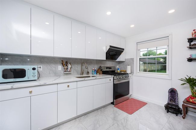 Kitchen with stainless steel gas stove, a sink, white microwave, light marble finish floors, and modern cabinets | Image 11