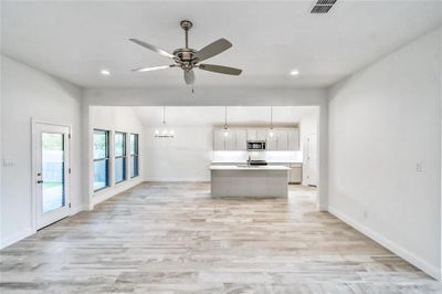 Kitchen featuring ceiling fan with notable chandelier, pendant lighting, a center island with sink, and light hardwood / wood-style floors | Image 2