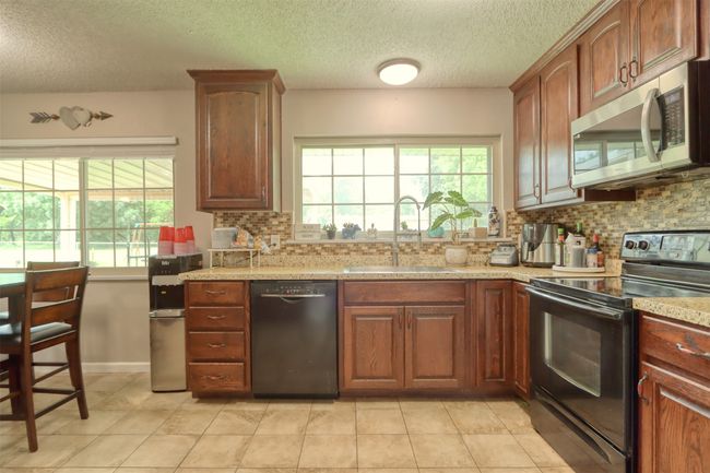 Kitchen featuring black appliances, backsplash, a textured ceiling, and light tile patterned floors | Image 20