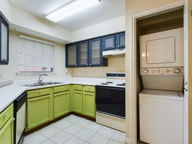 Kitchen featuring range with electric cooktop, a sink, white dishwasher, under cabinet range hood, and stacked washing maching and dryer | Image 9