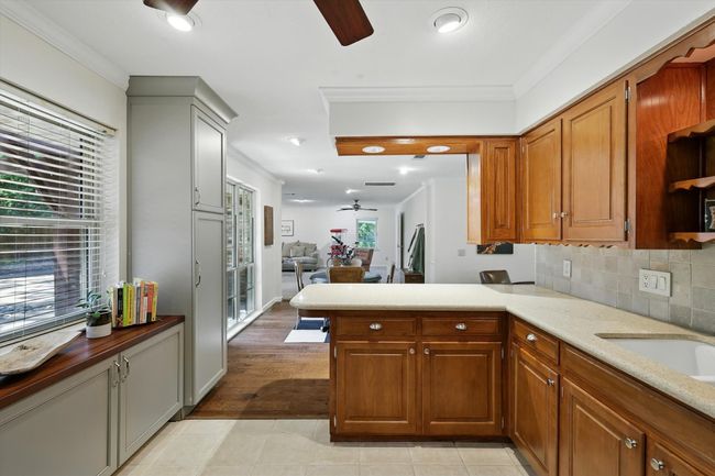 Kitchen featuring ceiling fan, ornamental molding, a peninsula, brown cabinets, and decorative backsplash | Image 11
