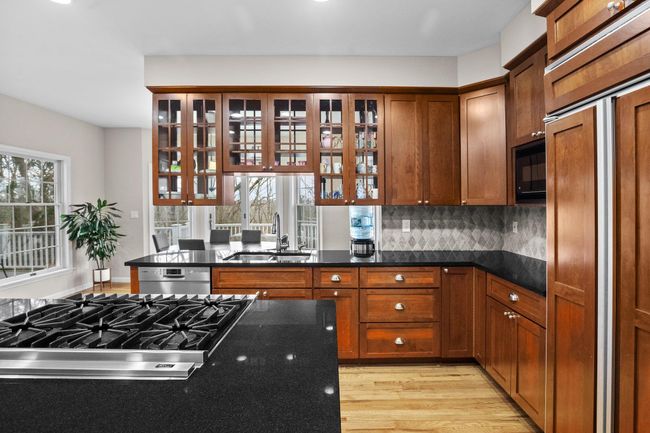 Glass-front cabinets, a large sink under triple windows, and premium finishes elevate both style and function in this upscale kitchen. | Image 4