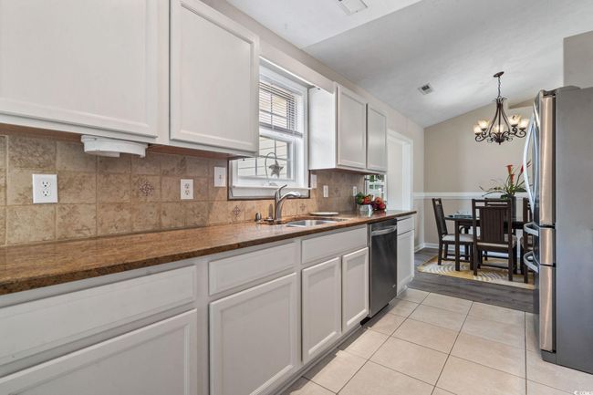Kitchen with appliances with stainless steel finishes, light tile patterned flooring, a chandelier, white cabinetry, and tasteful backsplash | Image 12