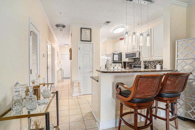 Kitchen featuring tasteful backsplash, light tile patterned flooring, white cabinetry, ornamental molding, and a peninsula | Image 8