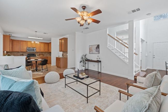 Living room with stairs, wood finished floors, a ceiling fan, baseboards, and a chandelier | Image 5