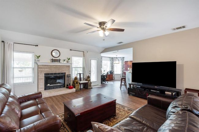 Living area featuring ceiling fan, a brick fireplace, wood finished floors, and visible vents | Image 5