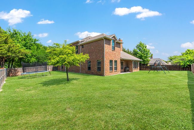 Back of property with a chimney, a fenced backyard, a lawn, brick siding, and a trampoline | Image 38