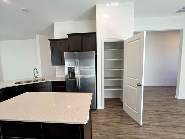 Kitchen with stainless steel fridge, dark wood-type flooring, light stone counters, and dark brown cabinetry | Image 13