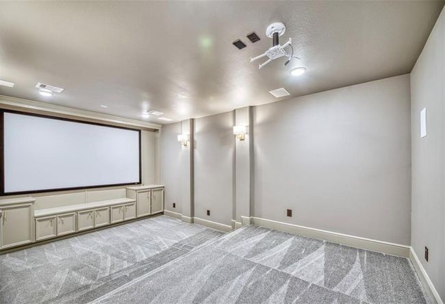This photo showcases a spacious home theater room with neutral-colored walls and ceiling. It features a large screen, built-in cabinetry, and wall sconce lighting, creating an ideal entertainment space. The room is carpeted, enhancing comfort and sound quality. | Image 35