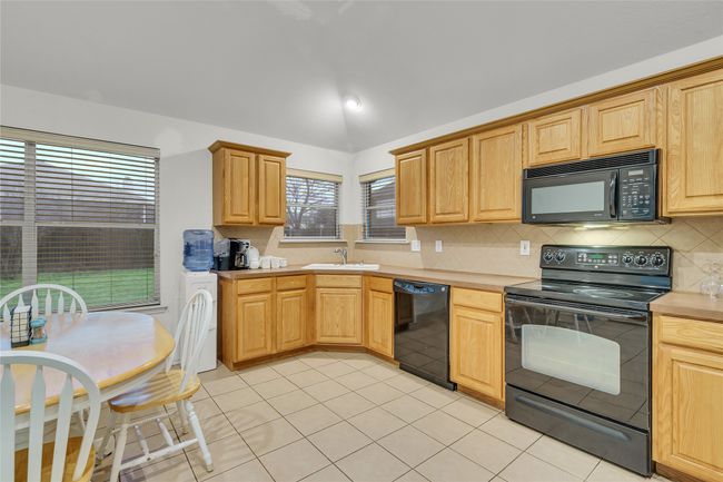 Kitchen featuring black appliances, light countertops, vaulted ceiling, backsplash, and light tile patterned flooring | Image 9