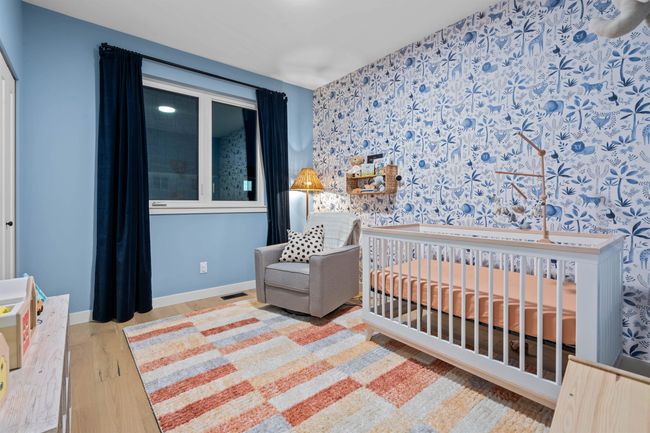 Bedroom with wallpapered walls, an accent wall, baseboards, wood finished floors, and a nursery area | Image 22