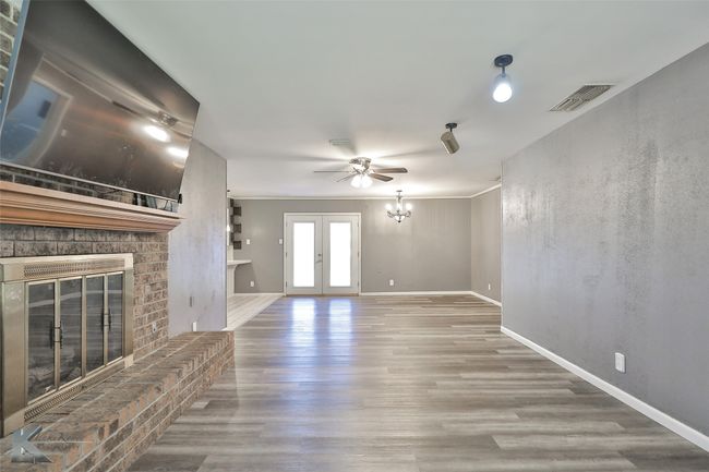 Unfurnished living room featuring french doors, a brick fireplace, ornamental molding, ceiling fan with notable chandelier, and wood-type flooring | Image 9