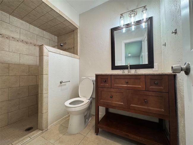 Bathroom with a walk in shower, vanity, toilet, tile patterned floors, and a textured wall | Image 13