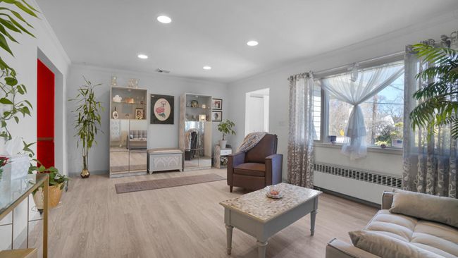 Living room with radiator heating unit, crown molding, light wood finished floors, and visible vents | Image 5