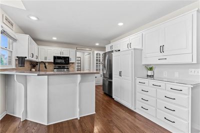 Kitchen featuring kitchen peninsula, white cabinetry, dark wood-type flooring, and appliances with stainless steel finishes | Image 2