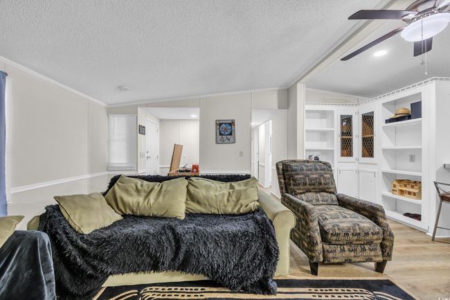 Living area featuring crown molding, a textured ceiling, a ceiling fan, wood finished floors, and lofted ceiling | Image 7