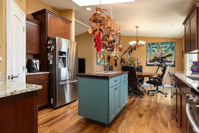 Kitchen with decorative light fixtures, stainless steel fridge with ice dispenser, dark stone countertops, a kitchen island, and light hardwood / wood-style floors | Image 9