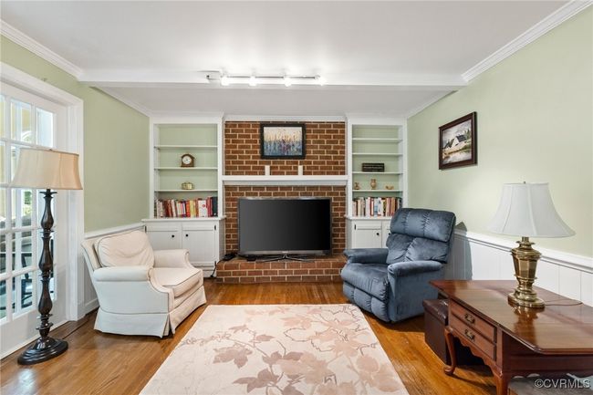 Living area with wood finished floors, a wainscoted wall, built in features, a fireplace, and ornamental molding | Image 24