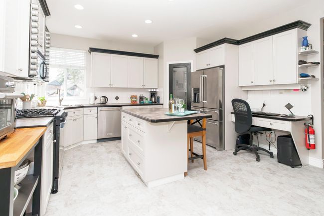 Kitchen with a kitchen island, a breakfast bar, appliances with stainless steel finishes, wood counters, and tasteful backsplash | Image 5