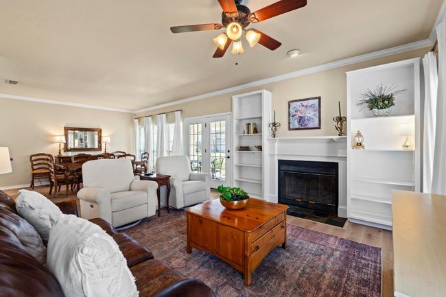 Living area featuring a fireplace with flush hearth, crown molding, ceiling fan, and wood finished floors | Image 6