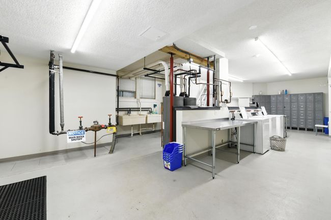 Well-maintained laundry area with multiple machines, stainless steel folding stations, lockers, and utility sinks. | Image 27