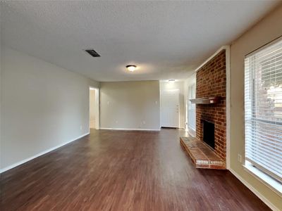 Unfurnished living room featuring a brick fireplace, a textured ceiling, and dark hardwood / wood-style floors | Image 3