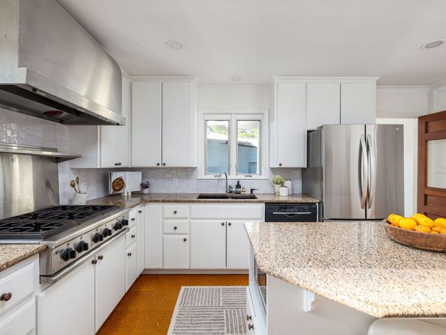 Kitchen with stainless steel refrigerator, kitchen island, & backsplash. | Image 10